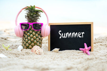 Summer in the party.  Hipster Pineapple Fashion in sunglass and listen music with blackboard on the sand beach beautiful blue sky background.  Fashion Summer Vacation Conceptの写真素材