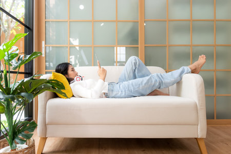 Home lifestyle woman relaxing lying down on sofa in living room. Happy girl play laptop comfortable pillows taking a nap for wellness and health in weekend holiday.  Lifestyle Conceptの写真素材