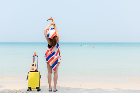 Summer vacations. Lifestyle  woman relax and chill on beach background.  Asia happy young people with bag travel suitcase luggage fashion dress raise arm wave sea, summer trips travelの写真素材