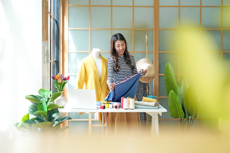 Asian young women fashion designer  working on her designer in the showroom,  Lifestyle Stylish tailor clothing design and cutting cloths in studio.  Business small Conceptの写真素材