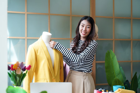Young women fashion designer using laptop working and design tailor and cloth in the showroom,  Lifestyle Stylish tailor taking measurements on mannequin for cutting cloths in studio.  Business and Industry small Conceptの写真素材