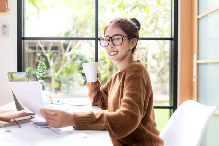 Young people work from home with laptop and drinking coffee in morning relax at home. Asia woman meeting conference connect online with office.  Business and Technology Conceptの写真素材