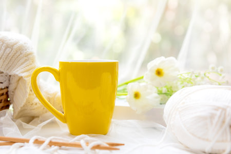 Coffee morning.  Yellow steaming cup of hot coffee for relax after working hobbies crochet on white wooden near window with flowersの写真素材