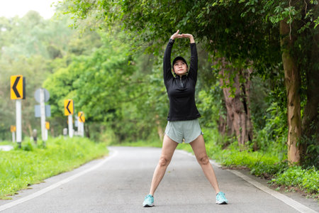 Healthy woman warming up stretching her arms and looking away in the road outdoor. Asian runner woman workout before fitness and jogging session at the park. Healthy and Lifestyle Conceptの写真素材