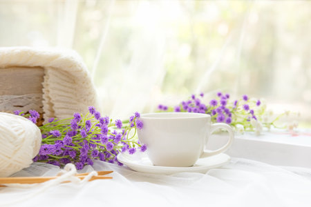 Coffee morning.  White steaming cup of hot coffee for relax after working hobbies crochet on white wooden near window with flowersの写真素材