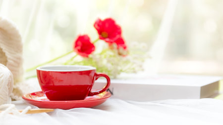 Coffee morning.  Red steaming cup of hot coffee for relax after working hobbies crochet on white wooden near window with flowers on autumn and winter seasonの写真素材
