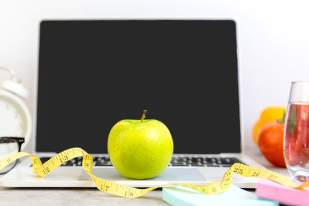 Close up green apple and tape measure.  Healthy snack for diet planning for working in office.  Fresh fruit dumbbell and laptop background.  Healthy Lifestyle Conceptの写真素材