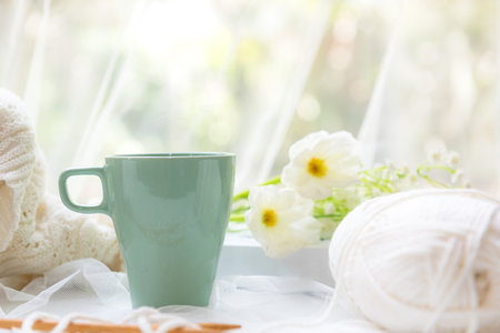 Coffee morning.  Green steaming cup of hot coffee for relax after working hobbies crochet on white wooden near window with flowersの写真素材