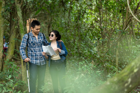 Asian couple traveler with backpack adventure holding map to find directions and walking relax in the jungle forest outdoor destination leisure explore education nature on vacationの写真素材