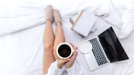 Asian woman in bedroom drinking coffee after wake up and relax mood in holiday near window, sunny morning. Young people chill and rest in white room backgroundの写真素材