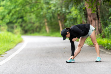 Healthy woman warming up before jogging run and relax stretching her arms and looking away in the road outdoor. Asian runner people workout fitness session, nature park backgroundの写真素材