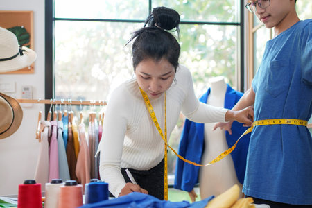 Asian women fashion designer  working and measure the customer in the showroom,  Lifestyle Stylish tailor clothing design and cutting cloths in studio.  Business small Conceptの写真素材