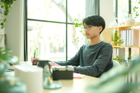 Asian teenage man using laptop for distance education and doing homework online.Â  Young man gamer playing broadcast game on the computer for relax and rest time.の写真素材