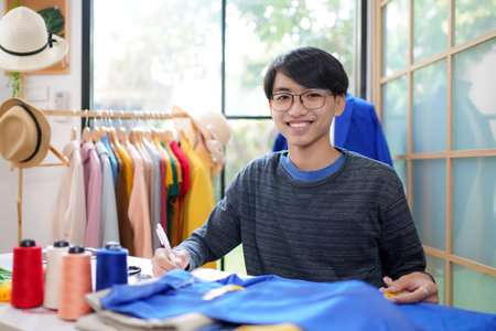 Trainee asian teenage man fashion designer  vocation and  education work on designer in the showroom,  Lifestyle Stylish tailor clothing design and cutting cloths in studioの写真素材