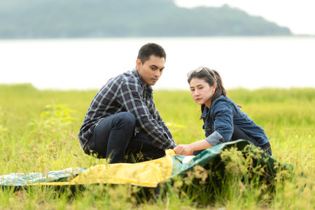 Friend helping installingÂ  tent camping outdoor near river and meadow.Â  Group young people family travel adventure destinationÂ leisure in vacations holiday.Â  Travel Conceptの写真素材