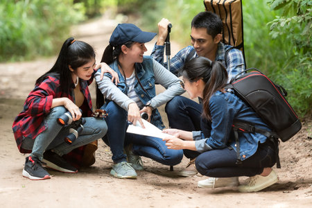 Group asian friends traveler with backpack adventure holding map to find directions and walking relax in the jungle forest outdoor for destination leisure explore education natureの写真素材