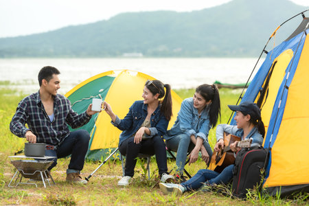Camping outdoor. Group  friends camping leisure and destination travel. Family sitting around camp fire and playing guitar and roasted sausages, tourism relax and travelの写真素材
