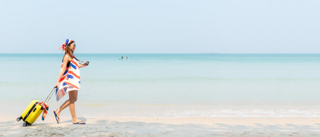 Summer vacations. Lifestyle woman talk a photo and relax chill on beach background.  Asia happy young people with yellow suitcase  fashion summerの写真素材