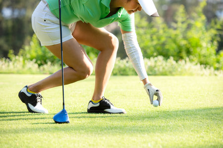 Asia sporty woman put golf ball on tee with club in golf course on evening on time for healthy sport. Banner and copy space for text.  Lifestyle and Sport Conceptの写真素材