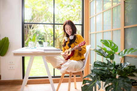 Young woman happy listen music for chill and playing guitar after finish work.   Lifestyle girl using laptop for meeting and working  in living room at home.  Lifestyle Conceptの写真素材