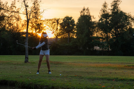 Golfer women sport course golf ball fairway. People lifestyle woman playing game golf approach teeoff on the green grass sunset background. Asian female player game shot in summerの写真素材