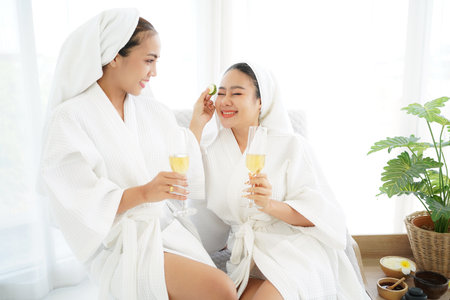 Asian women friends relaxing and enjoying spa massage with facial masks and bathrobes. Spa beauty...