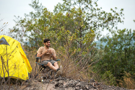 Lifestyle man travel hiker adventure and tent camping on mountain nature landscape. Young people tourist backpack drinking coffee in tent after activity outdoorの写真素材