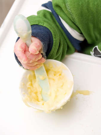 Caucasian baby's hand using spoon to eat mash potatoの写真素材
