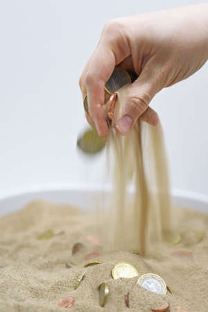 Abstract composition of spending money. Woman hand with coins and sand.の写真素材