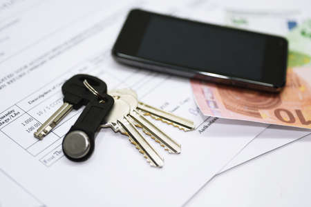 House key on a house shaped keychain resting on documents with mobile phone