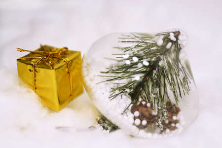 Macro photo of some Christmas objects. Yellow present with decorative cones in glass located on snow.の写真素材