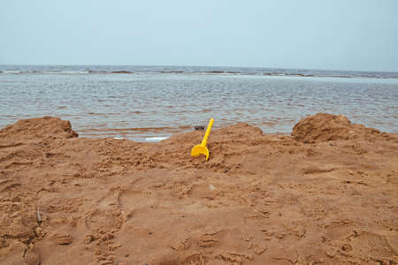 Yellow toy shovel in sand. Rainy day near sea.の写真素材