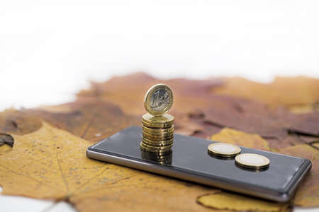 Smartphone on maple leaves background with some coins.の写真素材