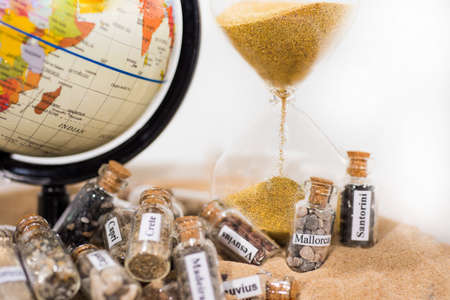 Glass test-tube with sand of different summer vacation countries. Located in sand with small globe and Hourglassの写真素材
