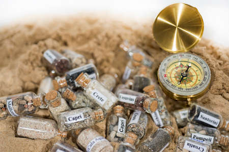 Glass test-tube with sand of different summer vacation countries. Located in sand with small compass.の写真素材