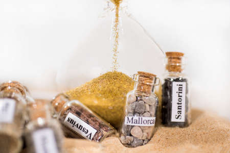 Glass test-tube with sand of different summer vacation countries. Located in sand with small globe...