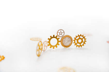 Clock gear wheels on white table with euro coins. Money currency abstract photo.