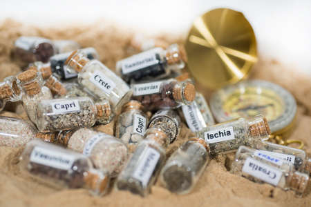 Glass test-tube with sand of different summer vacation countries. Located in sand with small...