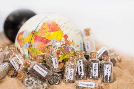 Glass test-tube with sand of different summer vacation countries. Located in sand with small globe.