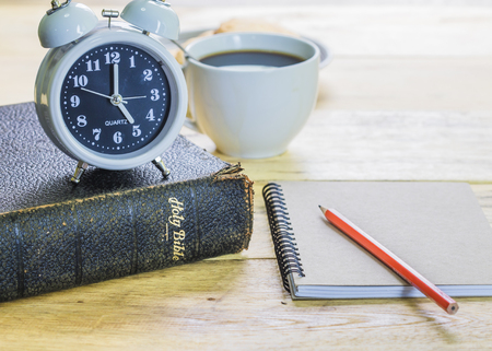 image of the old book with alarm clock, small note book, pencil and a cup of coffee on wooden...