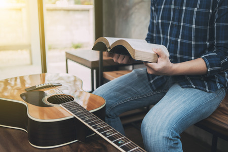 close up of a man hands holding  and read book  with guitar on wooden table, christian background, devotional conceptの写真素材