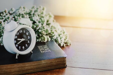Alarm clock on Holy bible with flowers on wooden table backgroundの写真素材