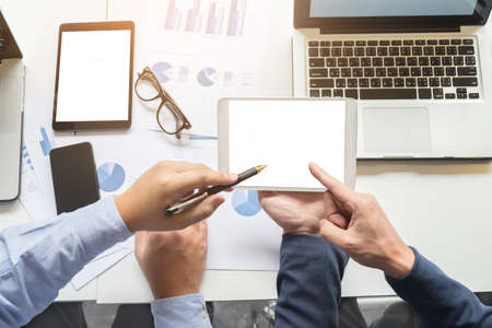Image of two young businessmen working with laptop, tablet, smartphone and financial document data graph on table in office.の写真素材