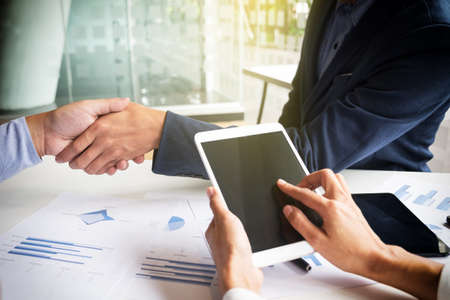 Teamwork concept of office working, Young business men shaking hands with document graph background.の写真素材