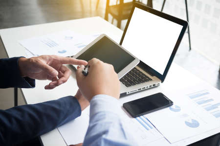 business documents on office table with smart phone and digital laptop and graph financial diagram and businessman working in the background.の写真素材