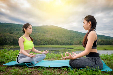 Two young womans sitting Yoga near river. Concept of healthy lifestyle and relaxation.の写真素材