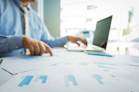Handsome young businessman working with laptop while sitting on the desk in office and financial...