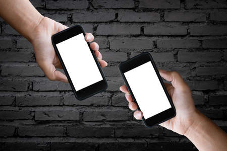 Two hands holding blank screen of a smartphone at the old black brick wall.の写真素材