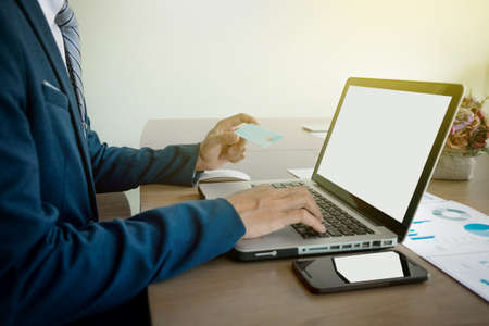 Man holding card in hand and entering security code using smart phone on laptop keyboard, online shopping concept.の写真素材