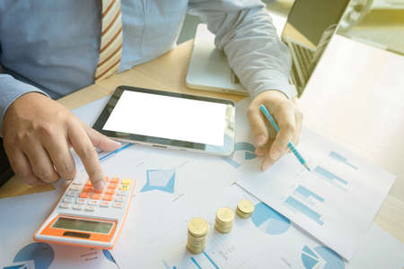 businessman using calculator with stacked coins arranged at office desk and many document data graph in morning light, business concept.の写真素材